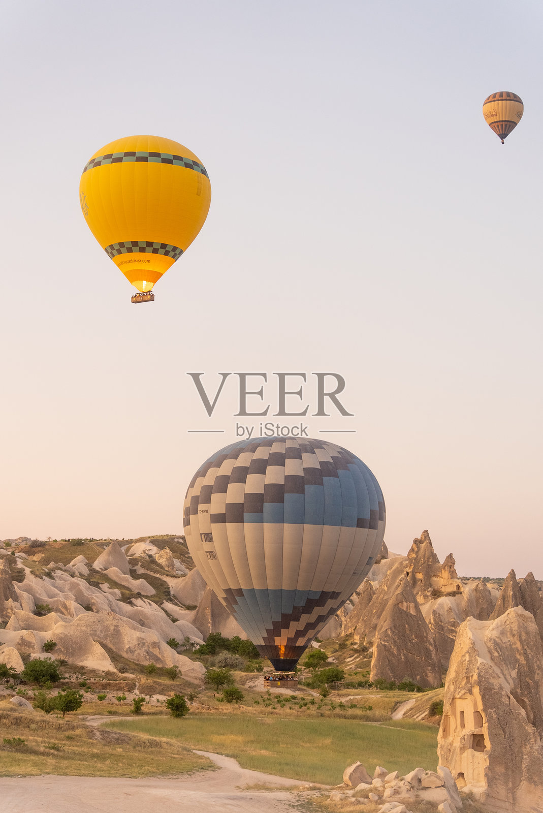 热气球在土耳其卡帕多奇亚的戈雷梅日出时飞越岩石 formations。照片摄影图片