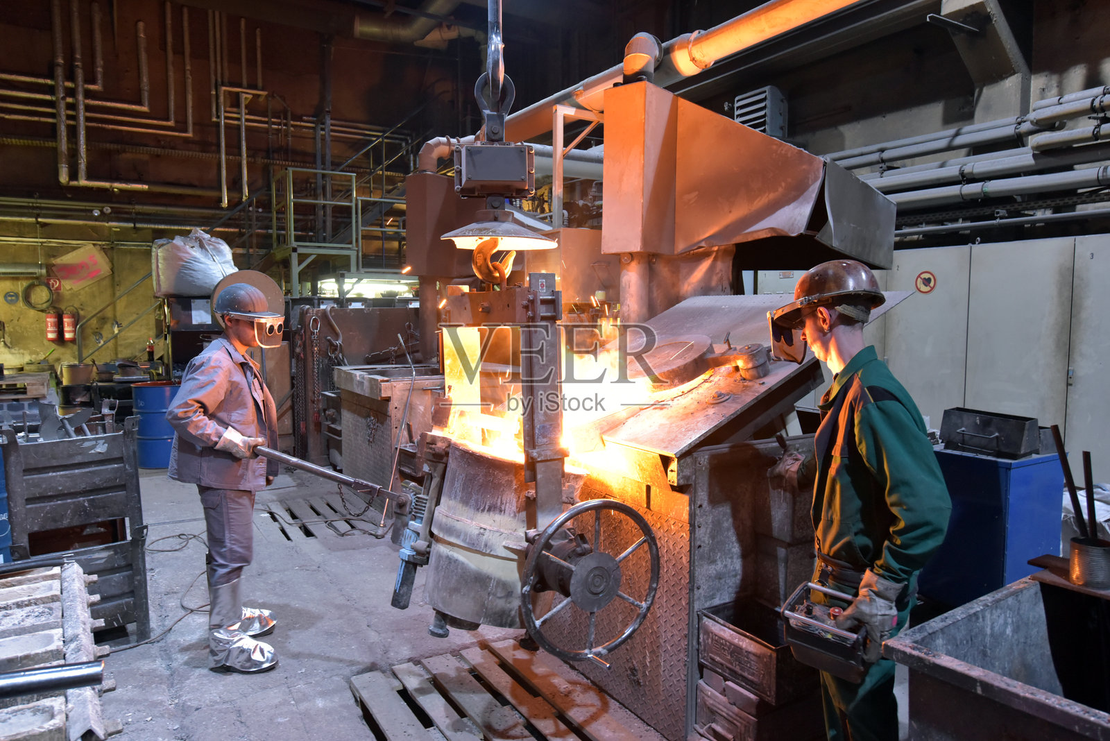 铸造厂的工人在铸造金属工件 - 工作安全与团队合作照片摄影图片