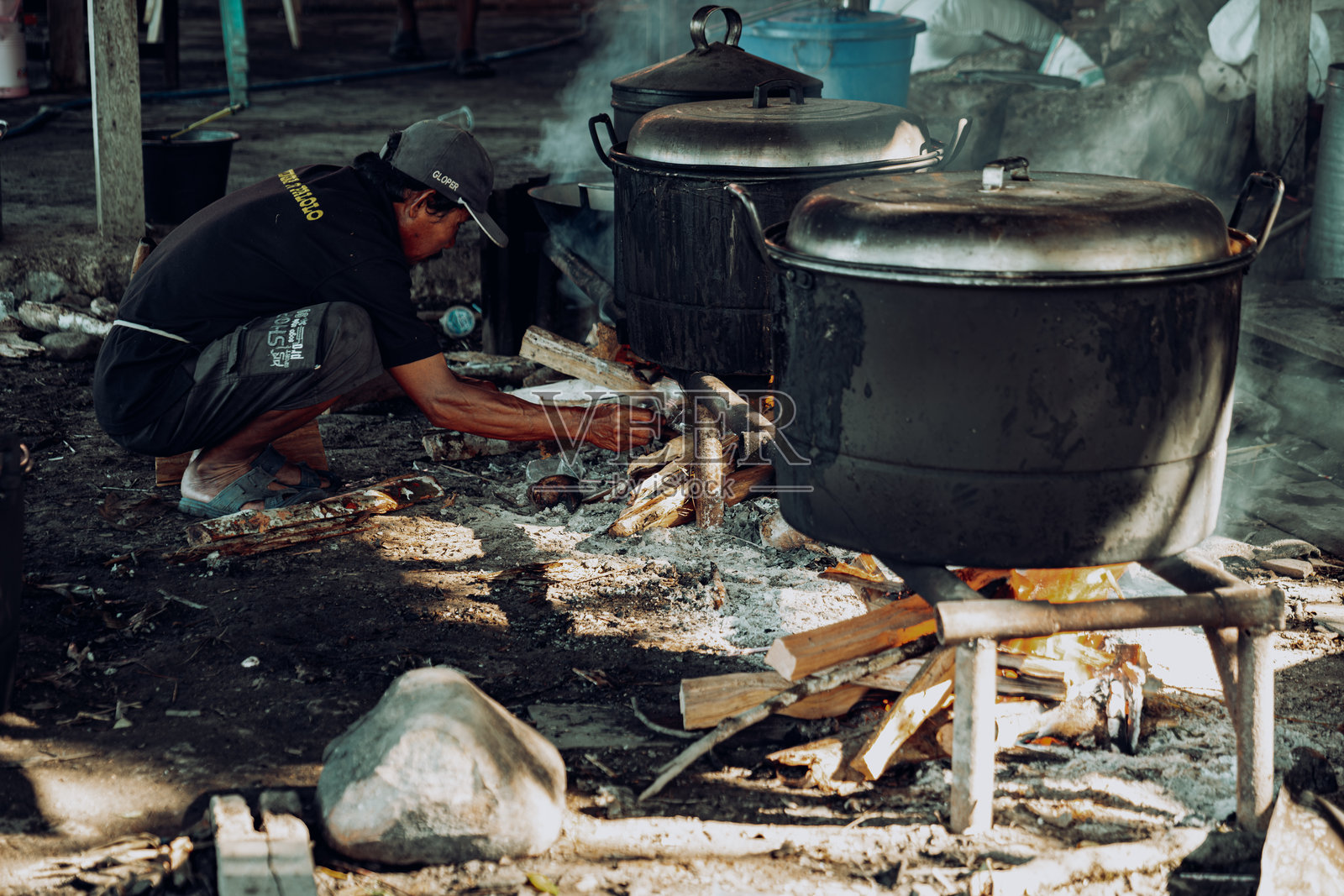 一个男人正在为大锅里的烹饪点燃柴火。照片摄影图片