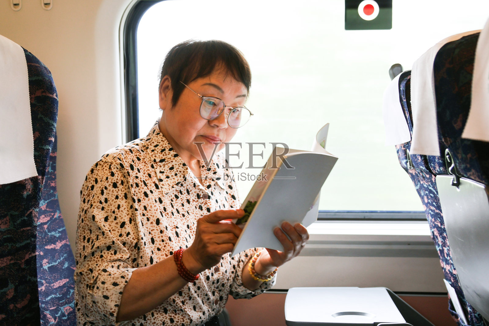 一位年长的亚洲女性在高铁上阅读一本书。照片摄影图片