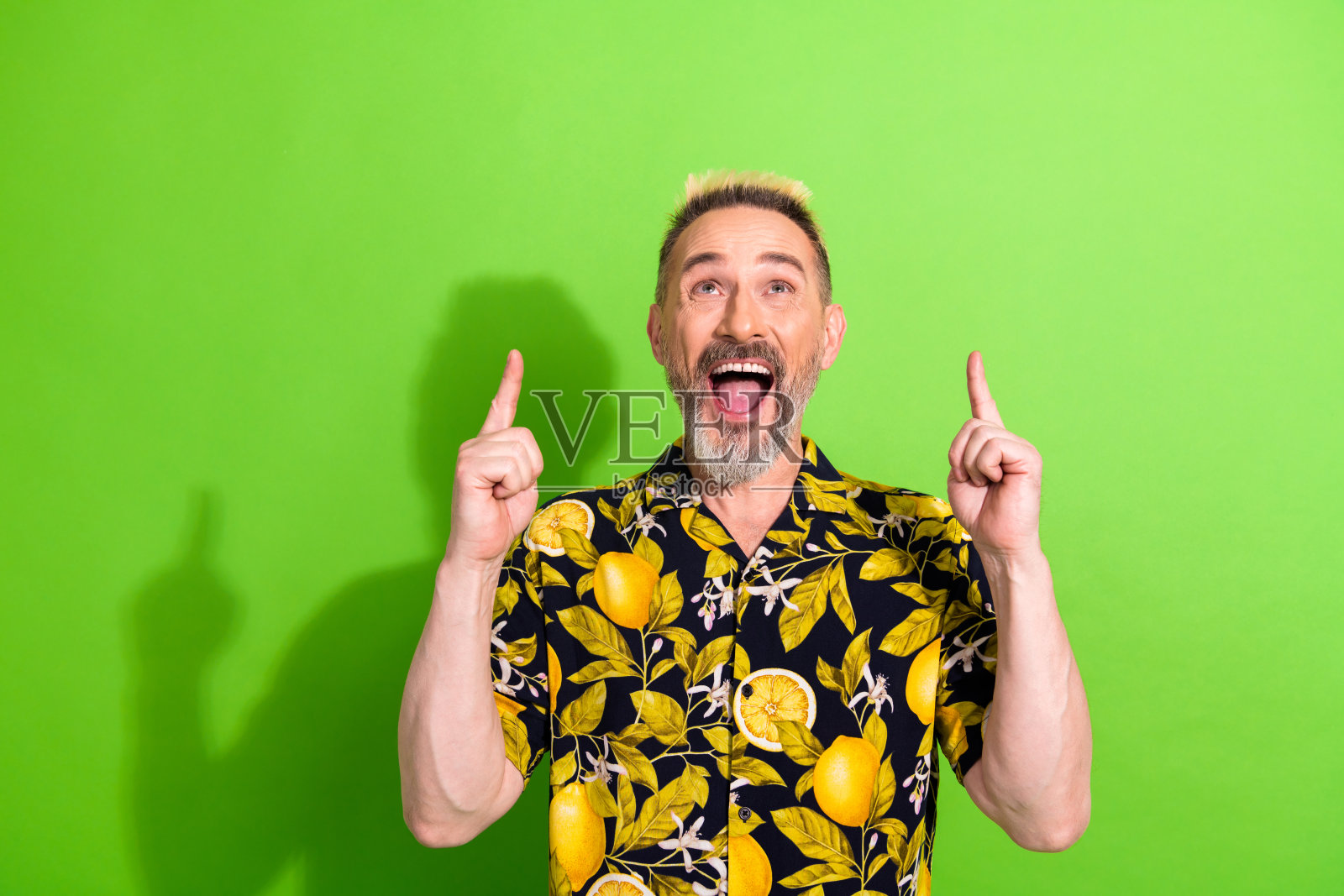 充满魅力的金发男子穿着鲜艳的热带衬衫，兴奋地在生动的绿色背景前摆姿势。照片摄影图片