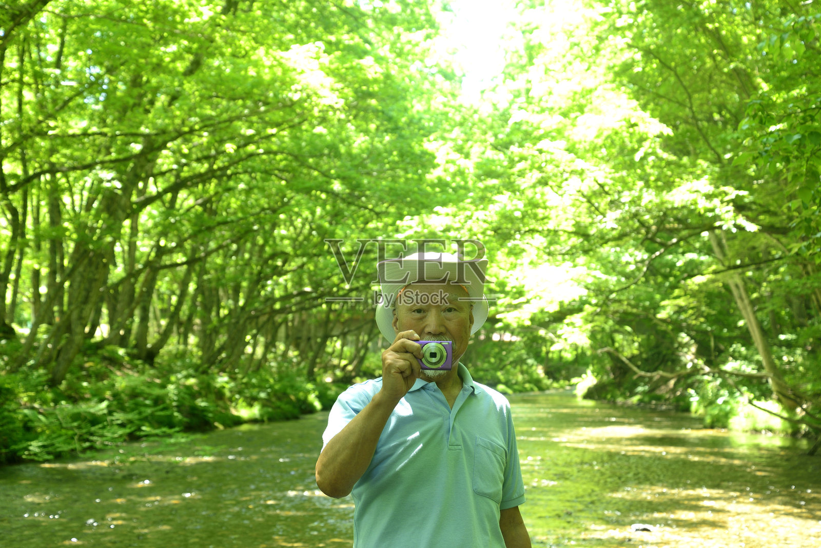 老年人在清澈的溪流旁用数码相机拍摄新鲜的绿意照片摄影图片