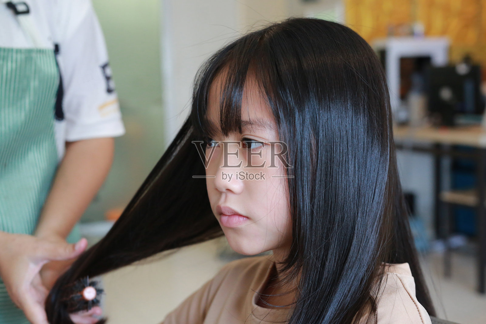 发型师在发廊为可爱的亚洲女孩做发型。年轻女孩在理发店。照片摄影图片