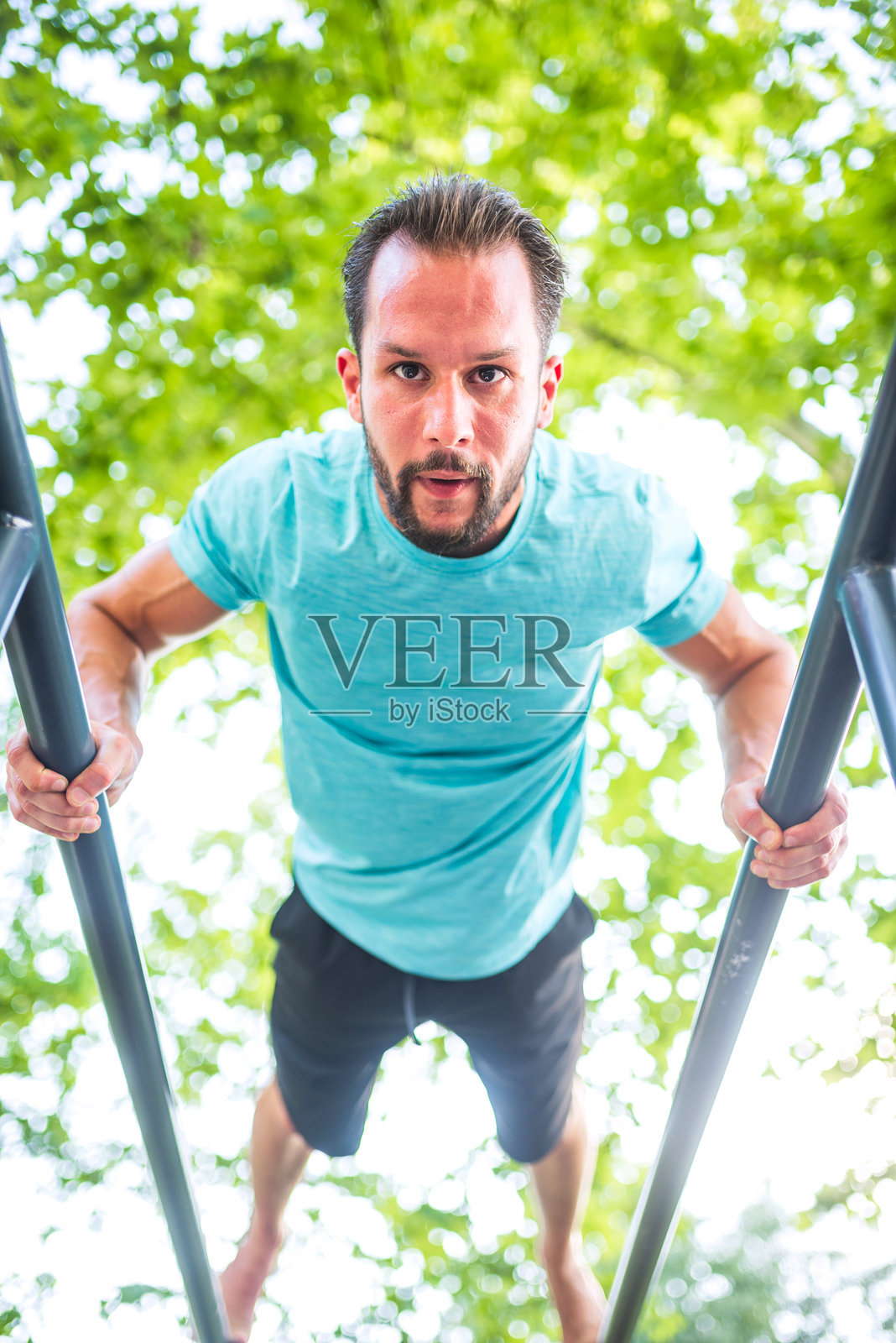 在公园里，坚定的男性运动员在双杠上做俯身撑。照片摄影图片