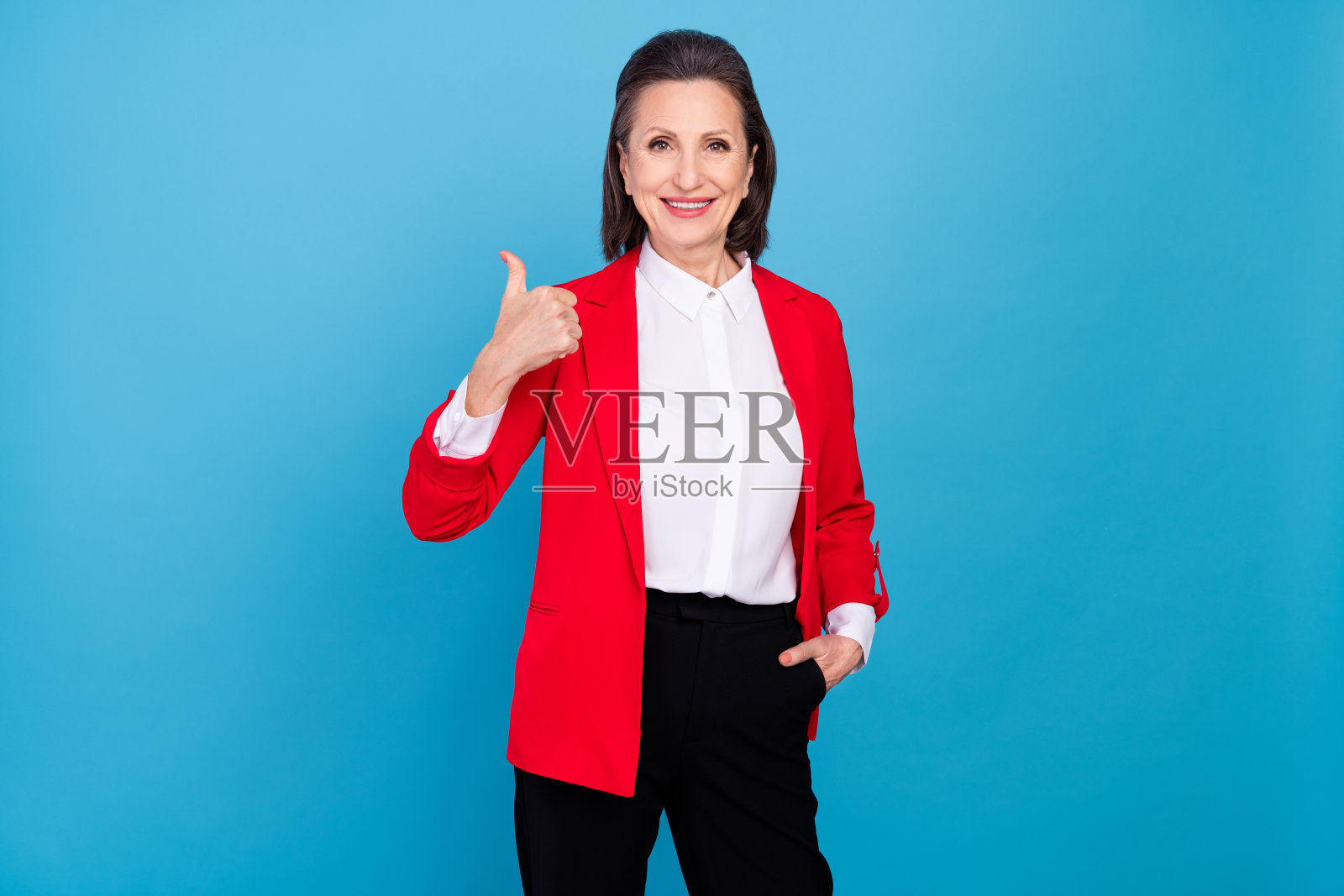 迷人的优雅快乐女商人雇主在明亮的蓝色背景前竖起大拇指。照片摄影图片