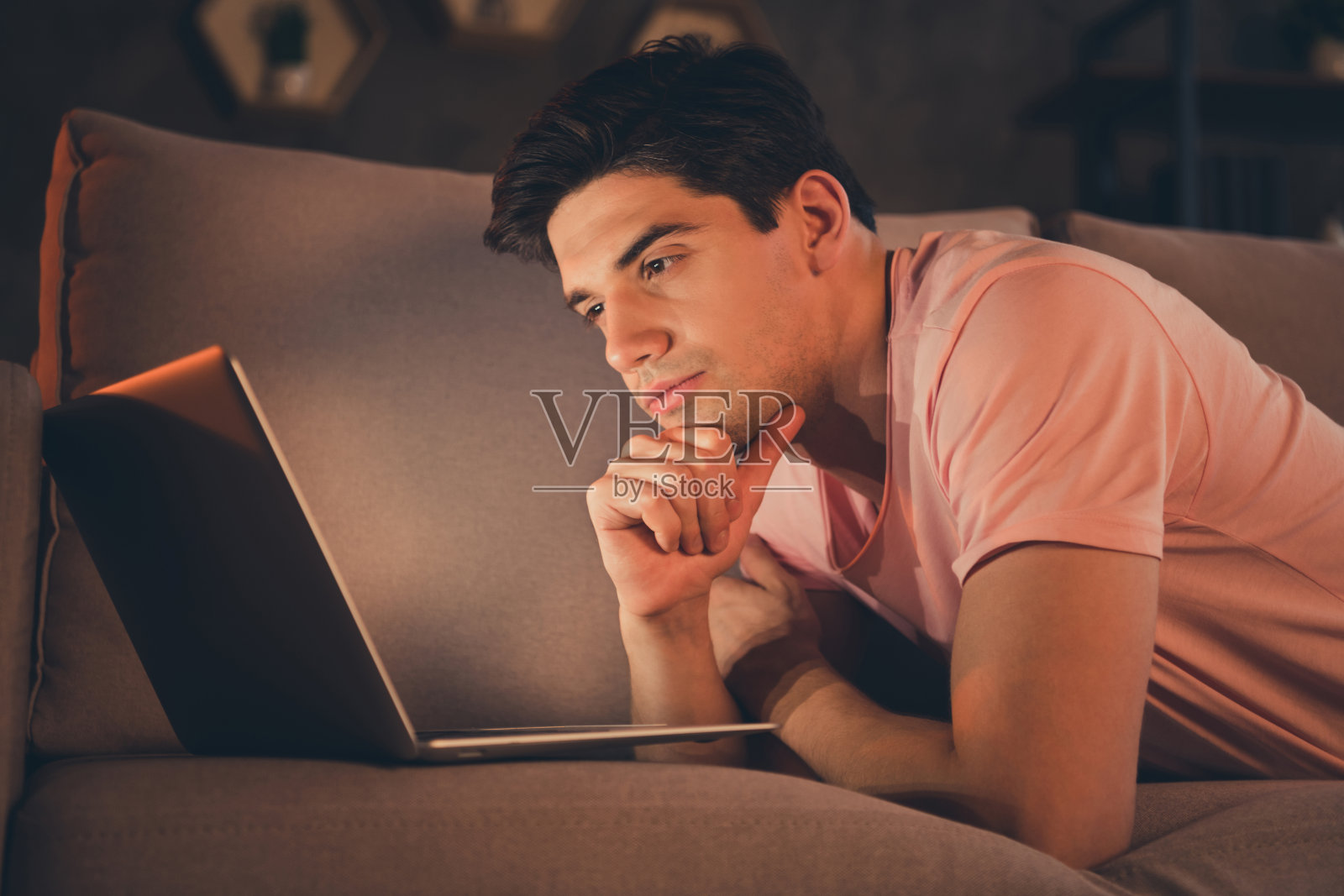 侧面视图的专注帅气男士躺在沙发上使用笔记本电脑阅读家庭室内的财务报告照片摄影图片