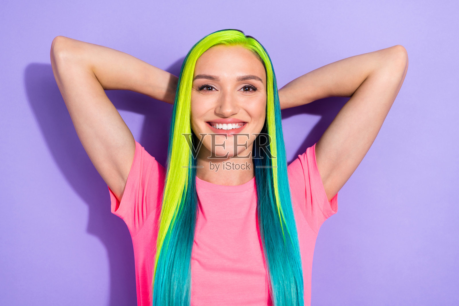 一位积极宁静的女士，五彩斑斓的发型，双手放在头顶，背景为紫色。照片摄影图片