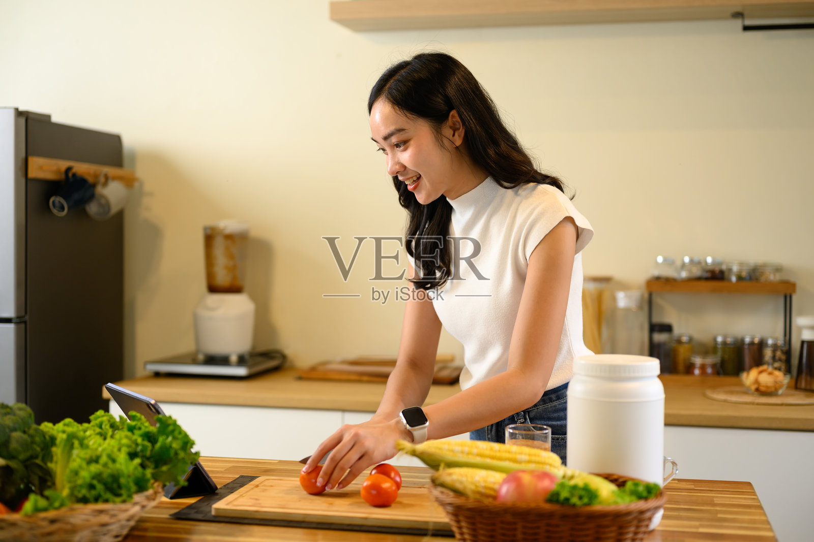 年轻女性切番茄并使用平板电脑查看烹饪说明照片摄影图片