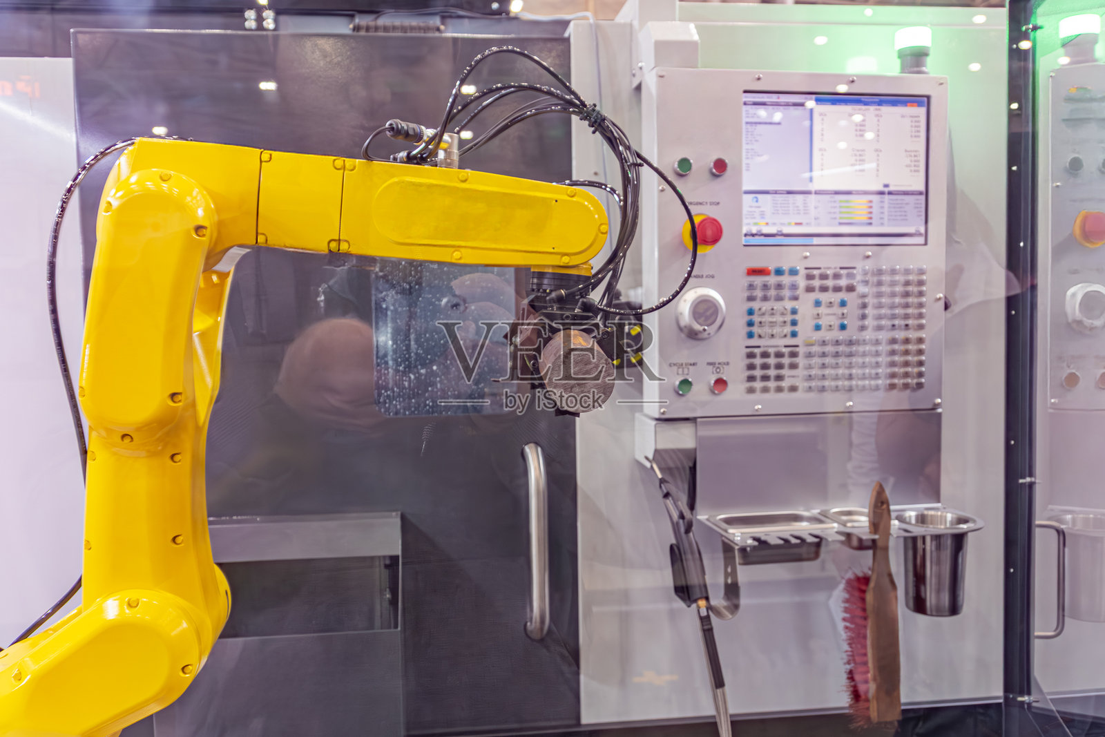 工业环境中的黄色机器人手臂，可能正在运作，部分可见的人戴着防护眼镜进行维护或监控，人工照明下的阴影，实用主义风格照片摄影图片