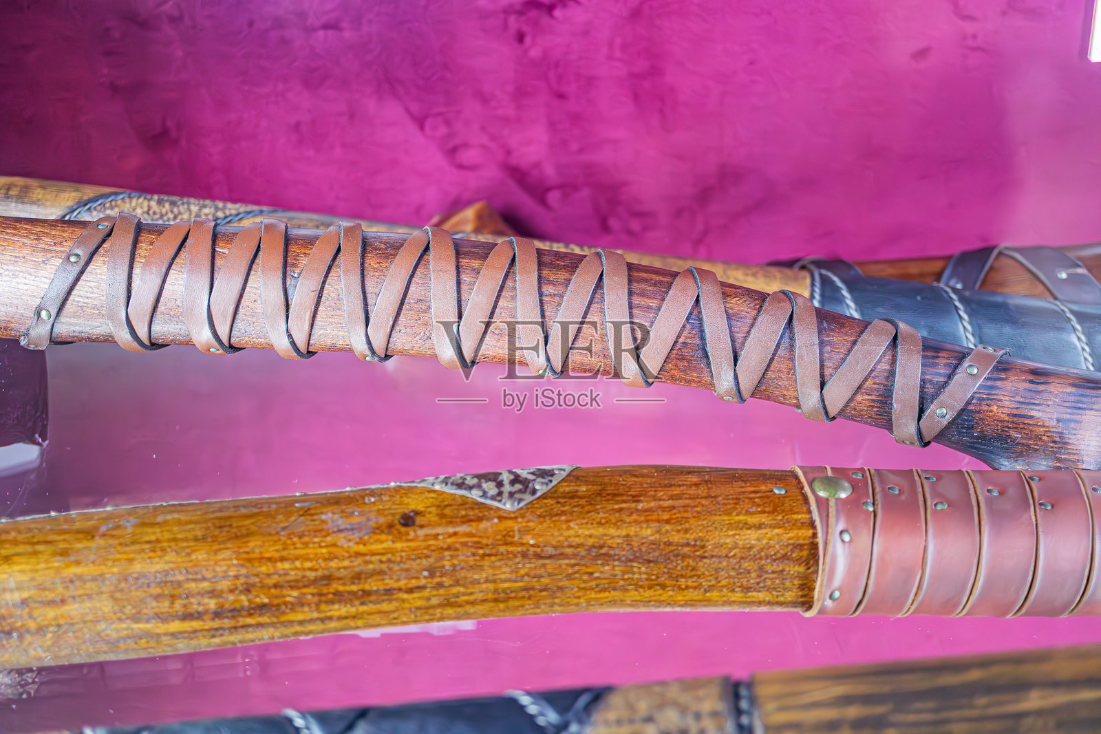 特写镜头展示一件古老的木制武器，精致的工艺，皮革包裹的手柄，背景为粉紫色，在柔和的室内灯光下。照片摄影图片