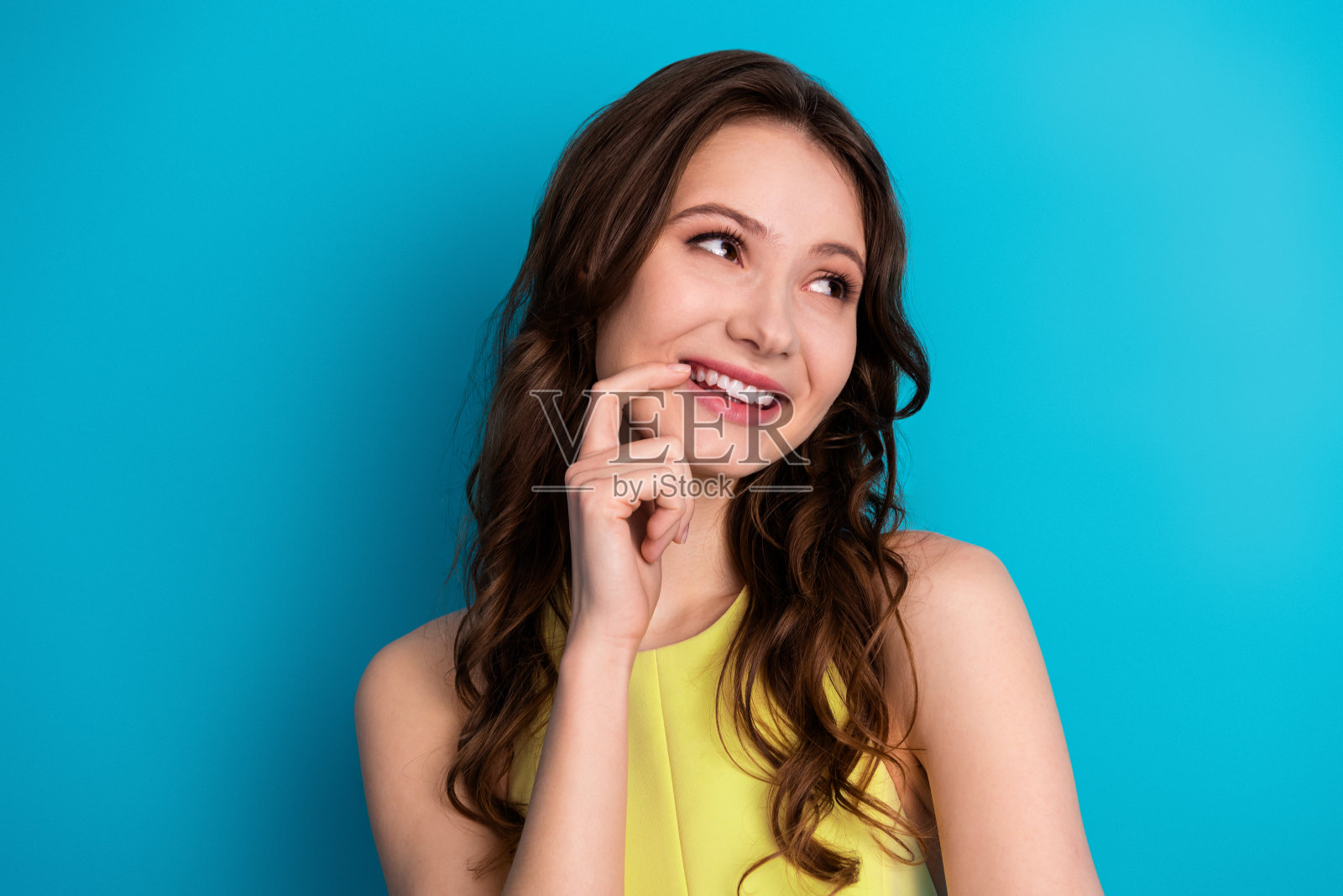 一位穿着时尚黄色连衣裙的年轻女性在鲜艳的蓝色背景前微笑，散发着自信和魅力。照片摄影图片