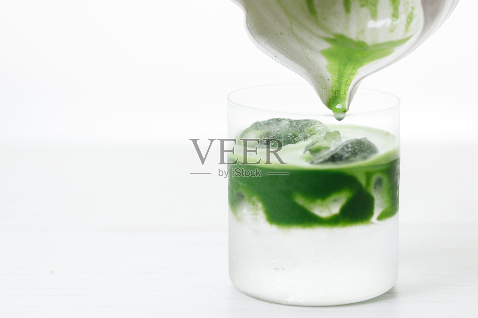 新鲜的抹茶茶，绿茶倒入一杯椰子水，放在白色木桌上。照片摄影图片