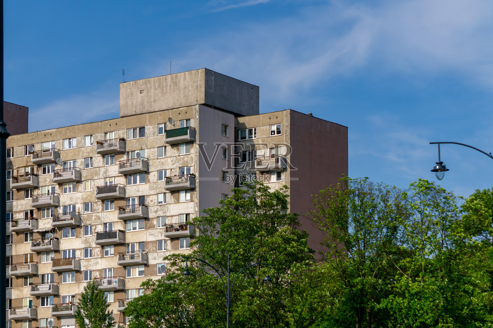 老旧的预制公寓楼，拥有众多阳台和空调，外立面风化，四周绿树环绕，拍摄于阳光明媚的日子。照片摄影图片