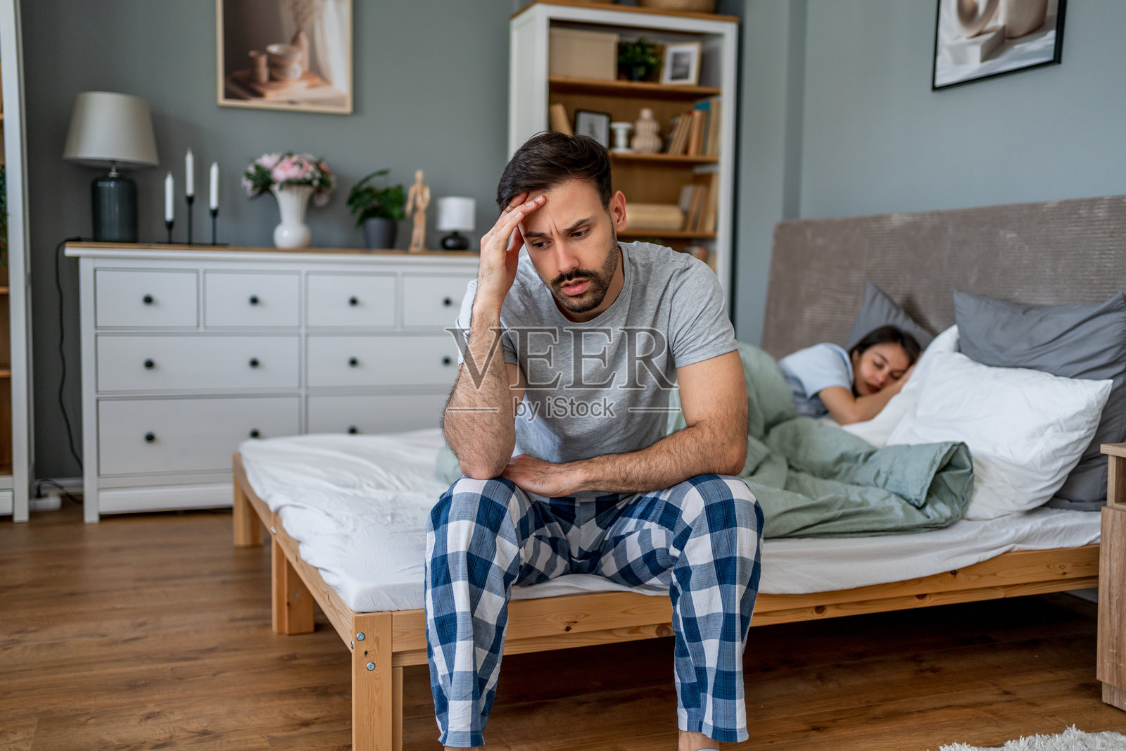 伤心的男人坐在床上，妻子正在睡觉。照片摄影图片