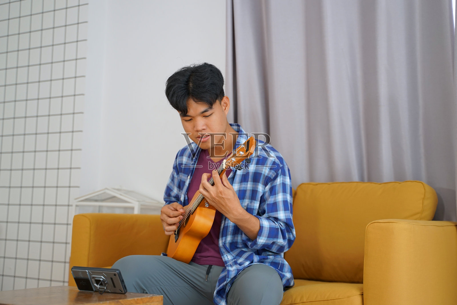 年轻男子在客厅里弹尤克里里。照片摄影图片