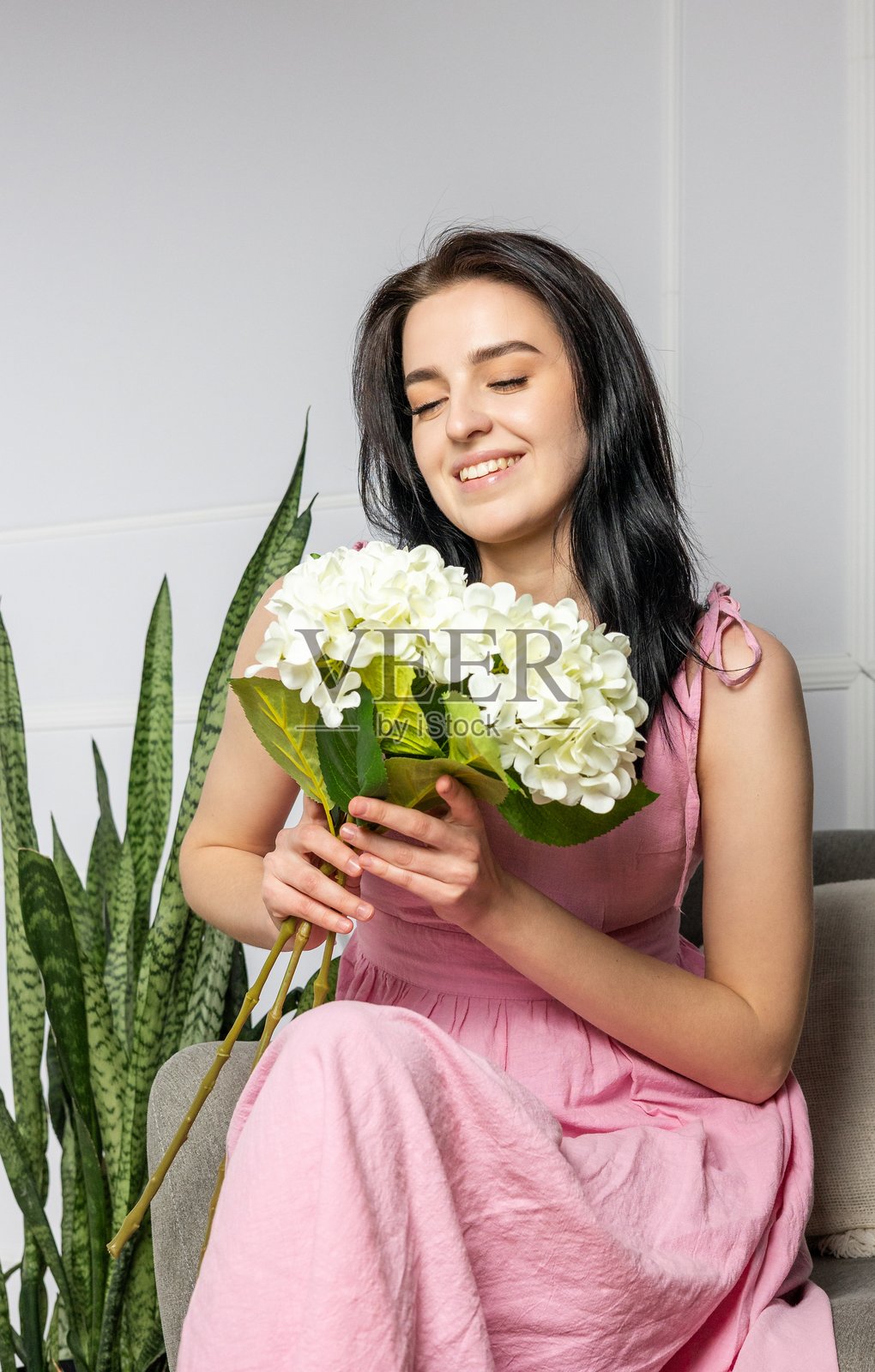年轻女性坐在明亮现代的室内，享受着一束白色花卉，周围有植物。照片摄影图片