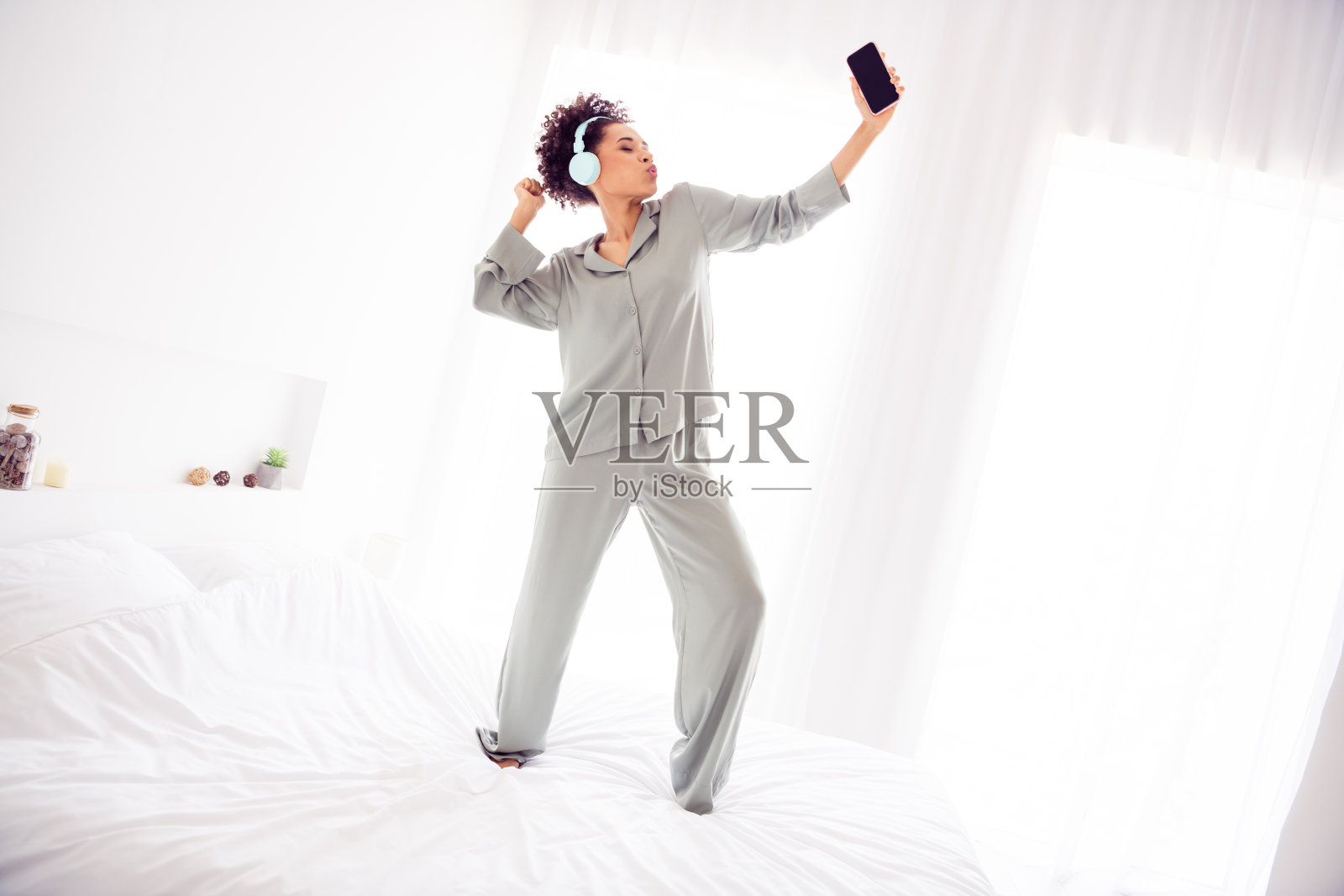 有趣的梦幻女士在卧室里穿着丝滑的睡袍，戴着耳机，边跳舞边吹口哨。照片摄影图片