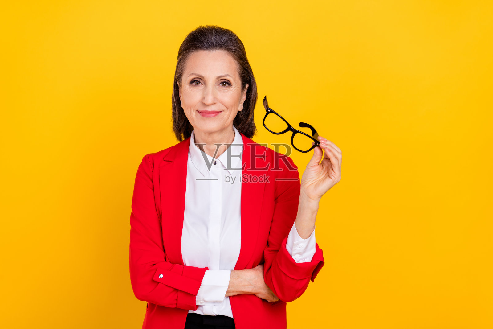 一位和蔼的深棕色头发的女士穿着红色夹克，试戴眼镜，背景为黄色。照片摄影图片