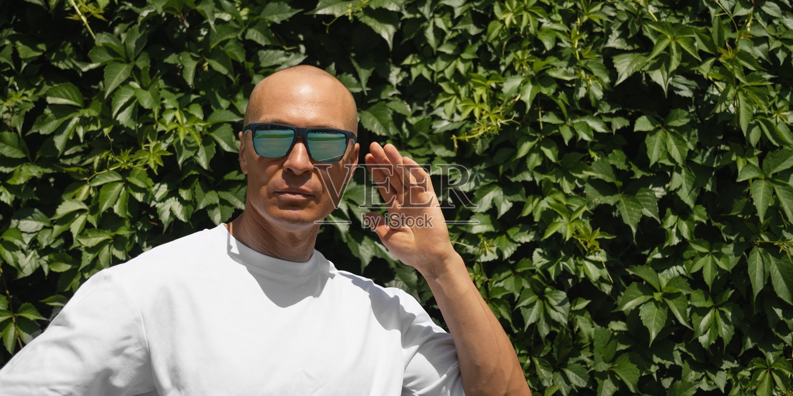 穿着T恤的白人男性在绿色植物墙前的户外肖像。生态概念。照片摄影图片