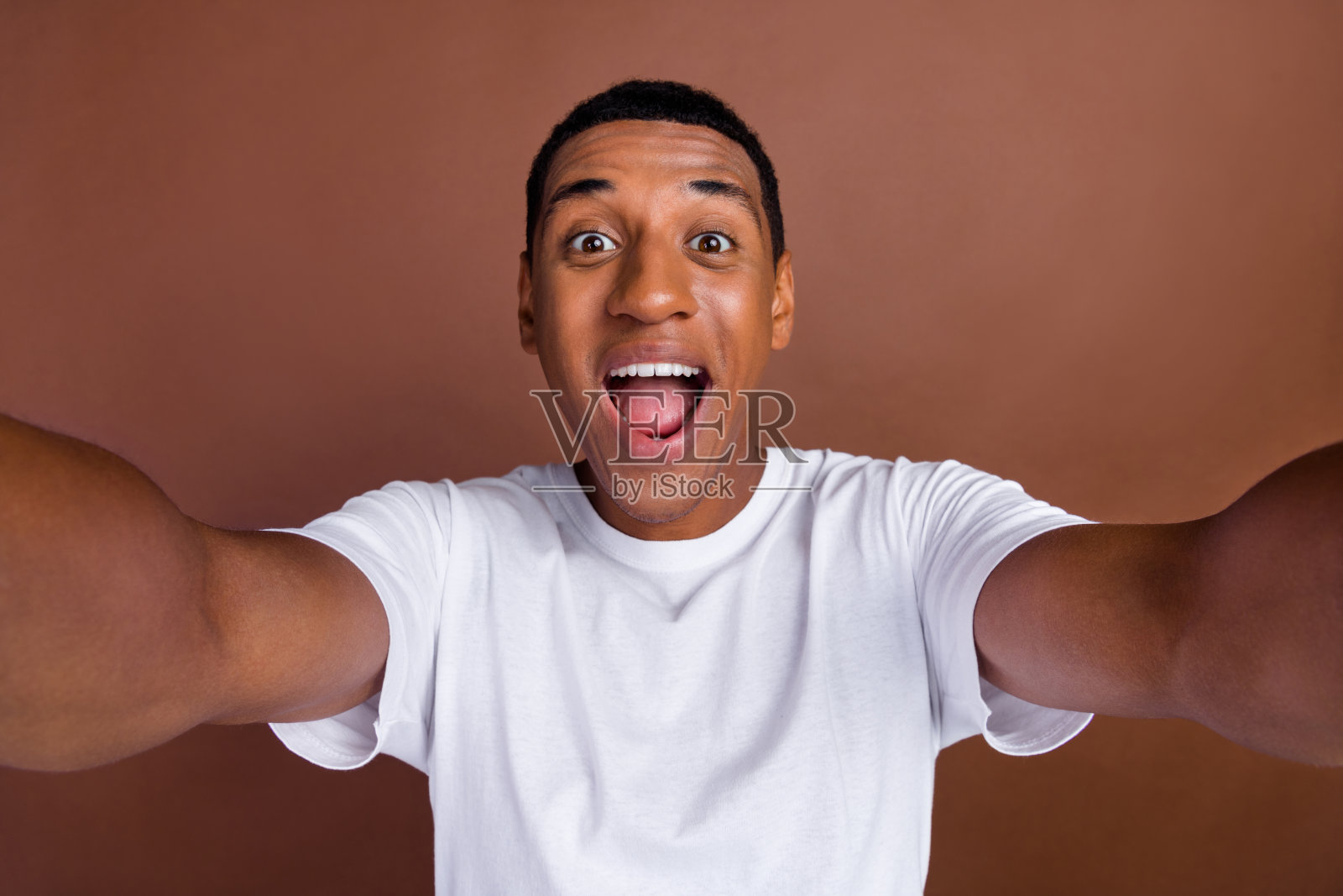 年轻兴奋的非洲裔男孩在棕色背景下拍摄自拍，惊讶的反应让人意外。照片摄影图片