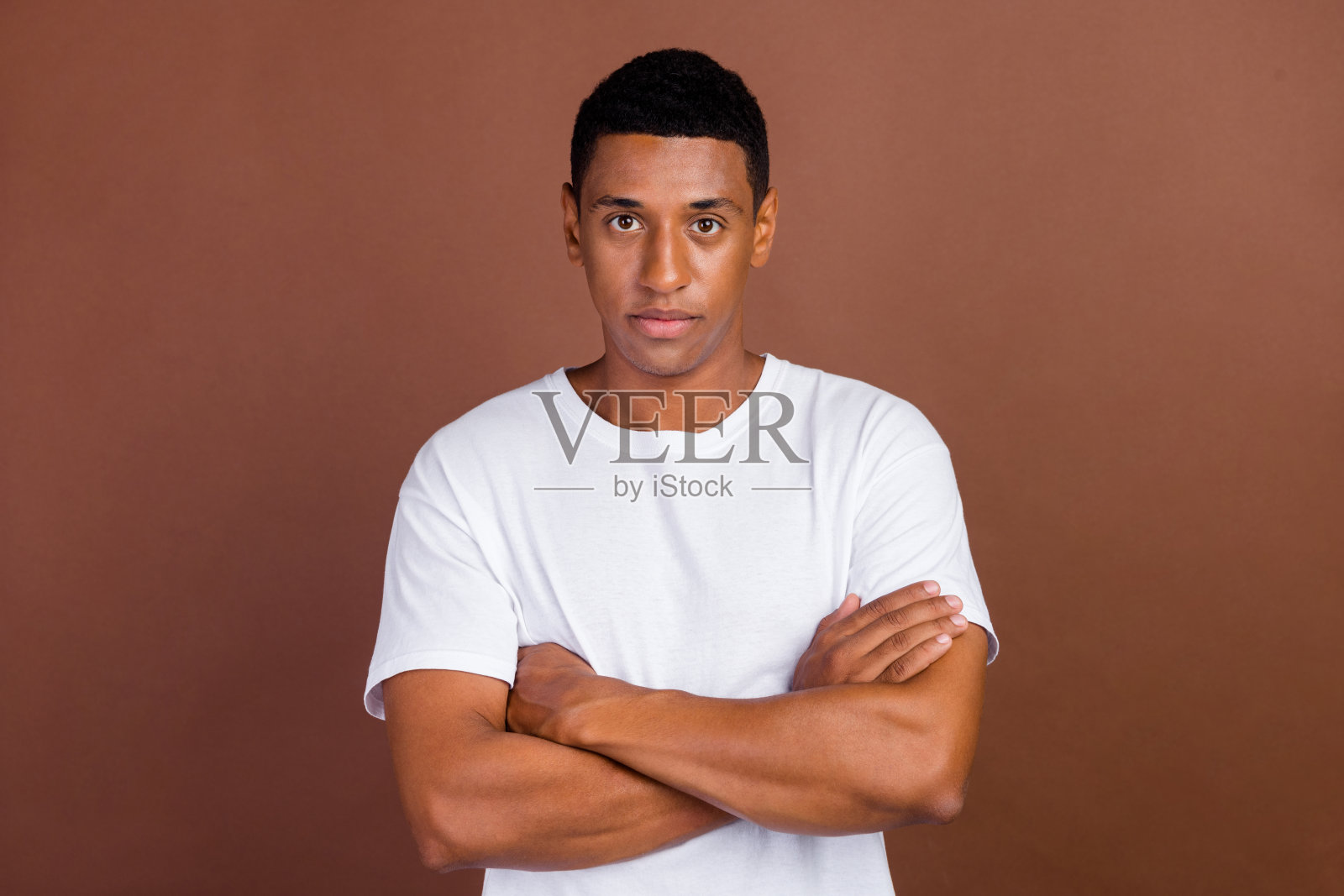 年轻非洲帅气男子双臂交叉，自信地穿着休闲服，背景为棕色。照片摄影图片