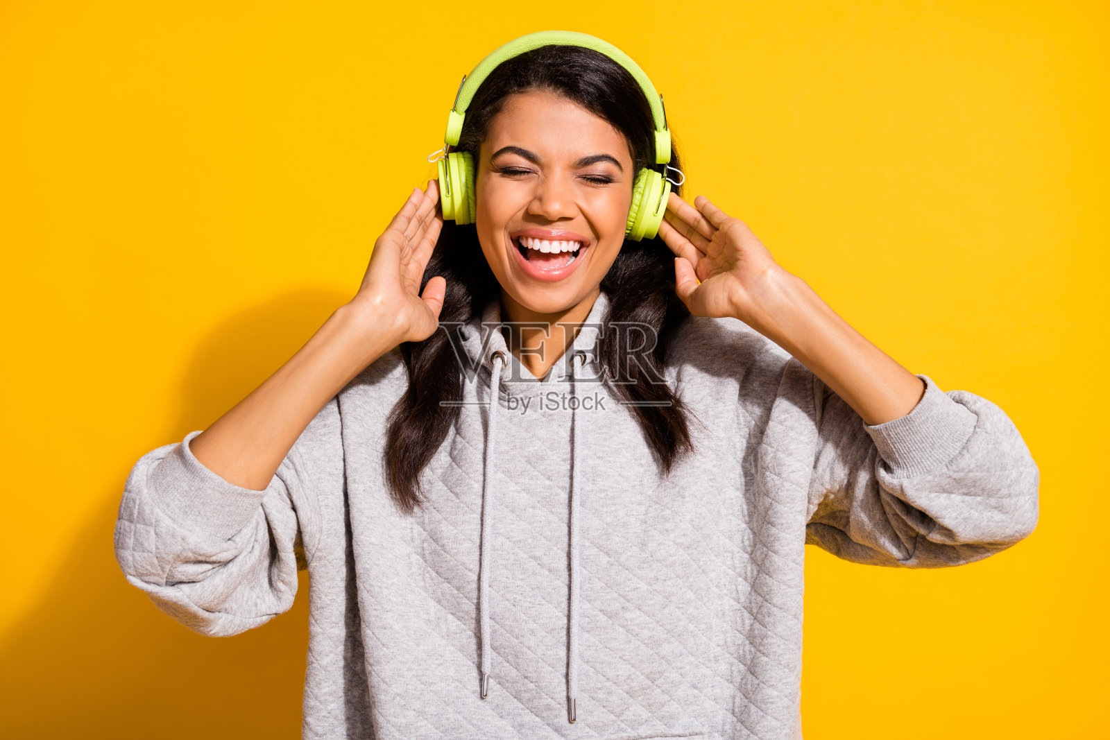 迷人的快乐深肤色女性戴着耳机，闭眼享受音乐，背景为黄色。照片摄影图片