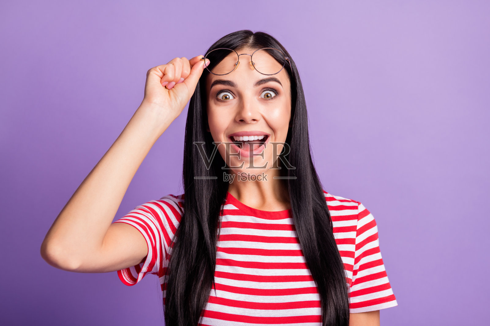惊讶的年轻女性手持眼镜，开心地购物，享受促销，背景为紫色。照片摄影图片
