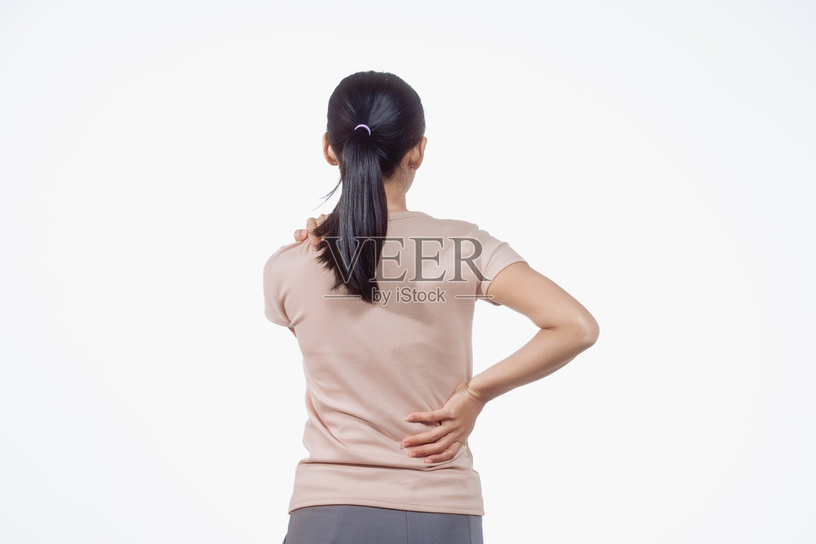 一位自信的年轻亚洲女性穿着浅棕色衬衫，站在白色背景前，感到颈部和背部疼痛。可能的原因包括肌肉拉伤、椎间盘问题或脊柱疾病。照片摄影图片
