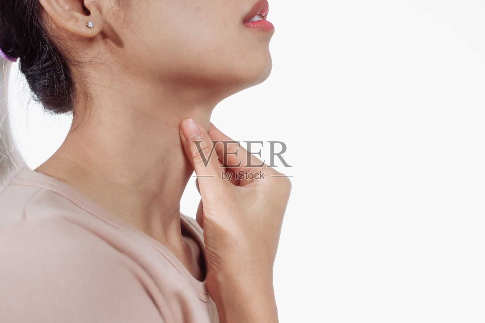 一位自信的年轻亚洲女性穿着浅棕色衬衫，站在白色背景前，感到喉咙痛。她可能患有常见的鼻喉疾病，如感冒、过敏或鼻窦炎。照片摄影图片