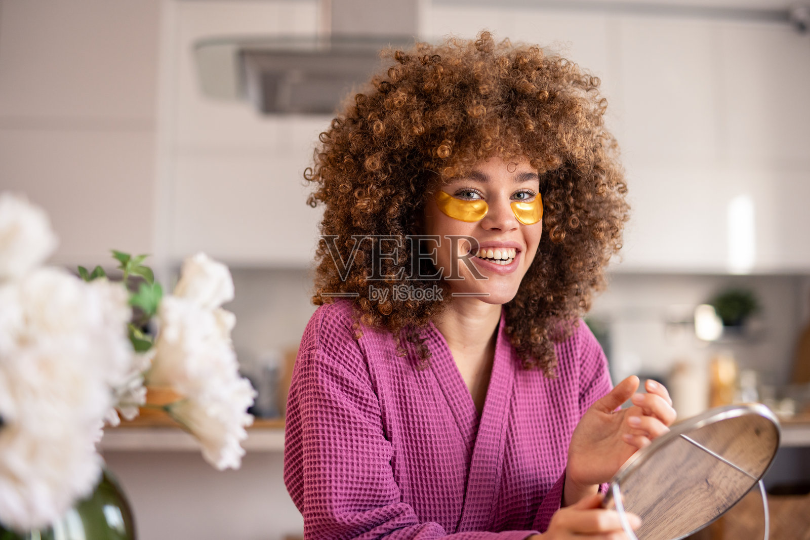 愉快的白人女性穿着粉色浴袍，在明亮的自然光下室内进行护肤。照片摄影图片