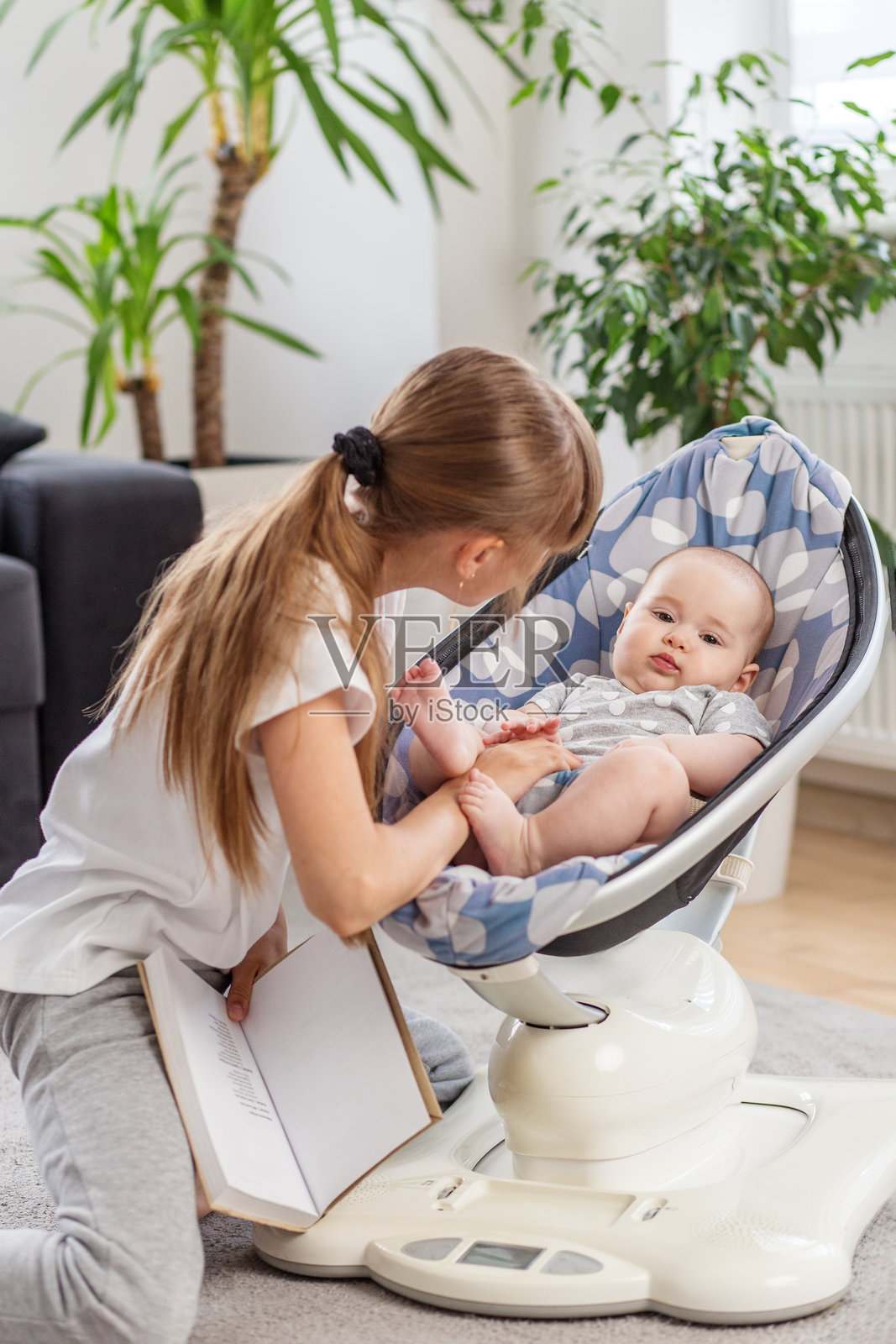 姐姐在摇椅上用书安慰婴儿照片摄影图片