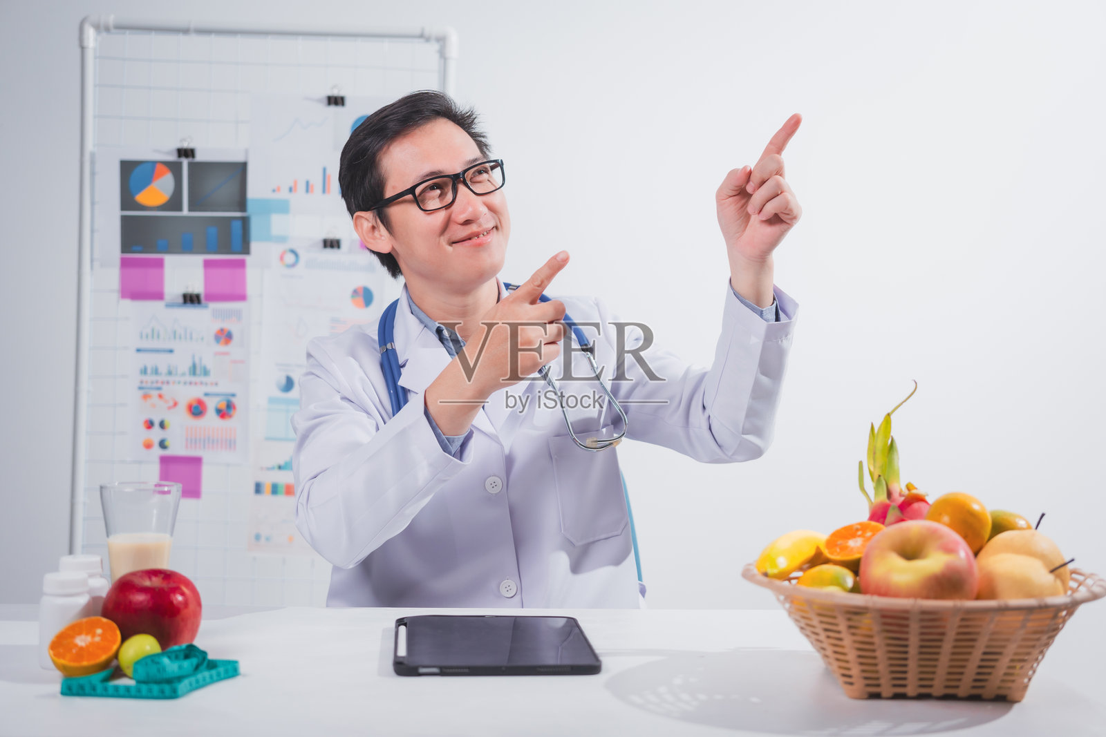 一位男性营养师在桌前工作，讨论吃水果的好处。他分析饮食并教育患者健康饮食习惯，以实现最佳健康和福祉。照片摄影图片