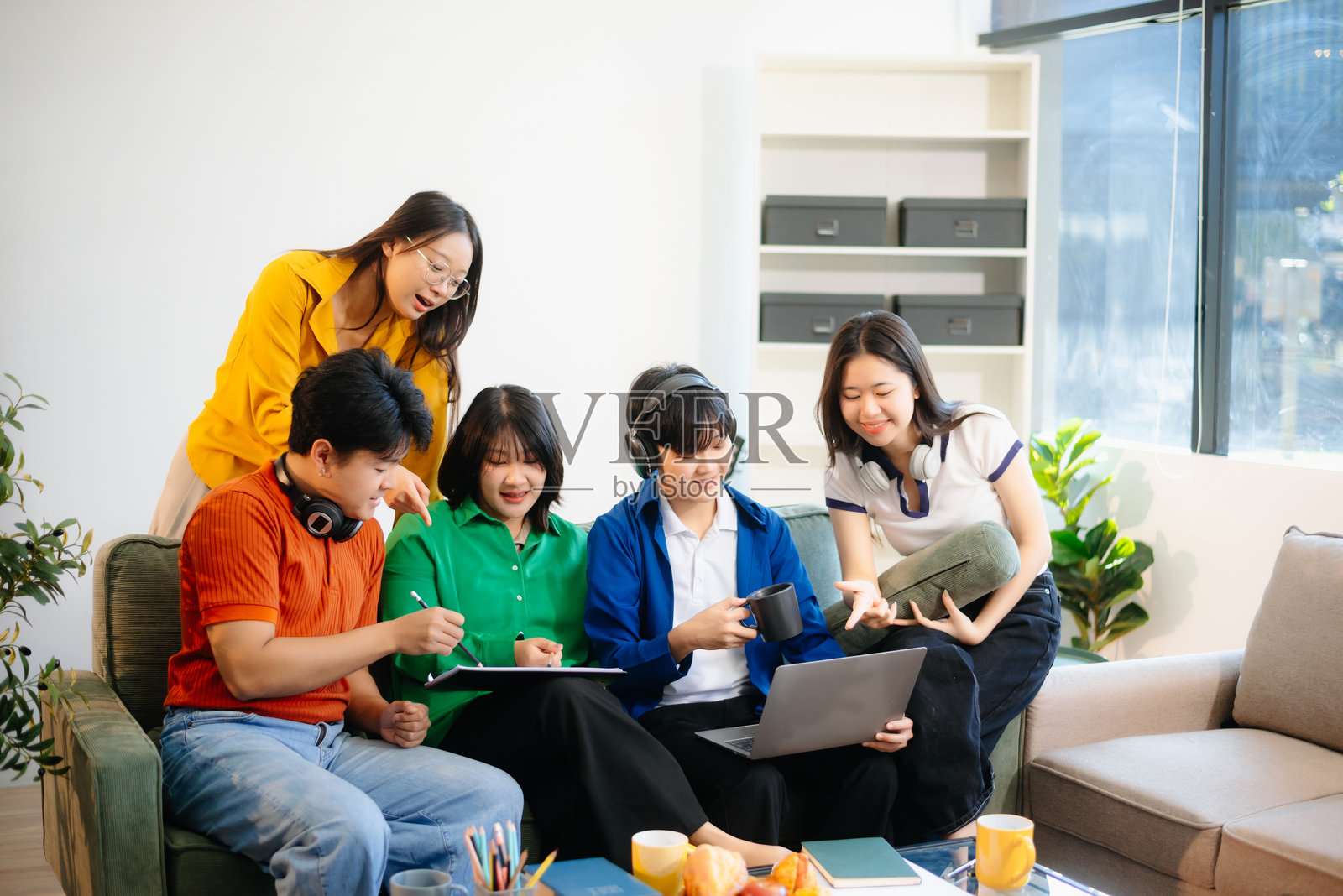 一群年轻的亚洲学生在舒适的室内环境中使用笔记本电脑和平板电脑合作完成项目，展现团队合作精神。照片摄影图片