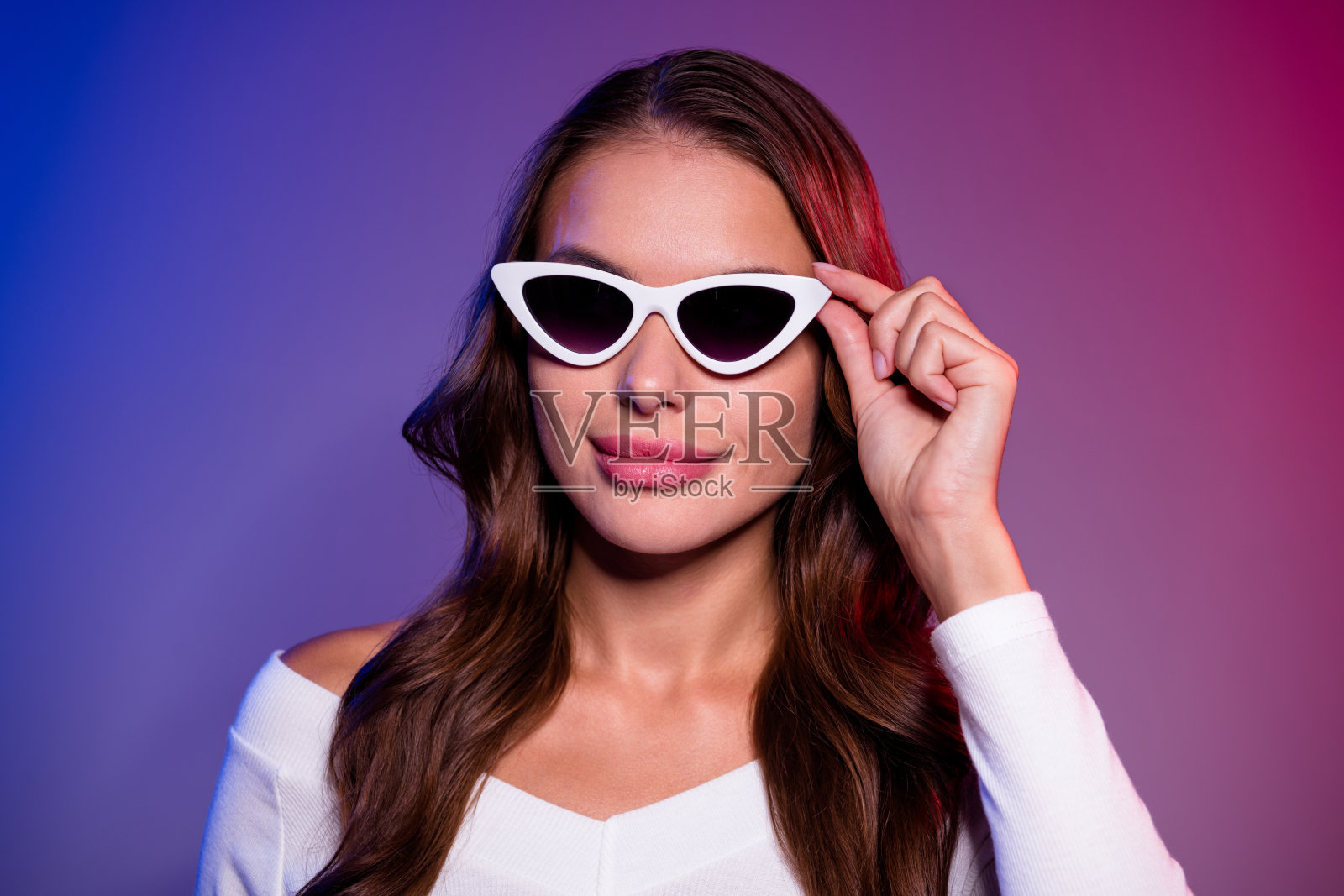 梦幻般的酷炫年轻女性，穿着白衬衫，戴着深色眼镜，微笑着，背景为渐变蓝红色，空旷的空间。照片摄影图片