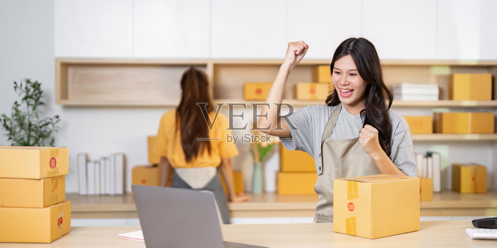 小型企业成就。一位女性在她的创业工作空间中庆祝成功，周围有包裹。照片摄影图片