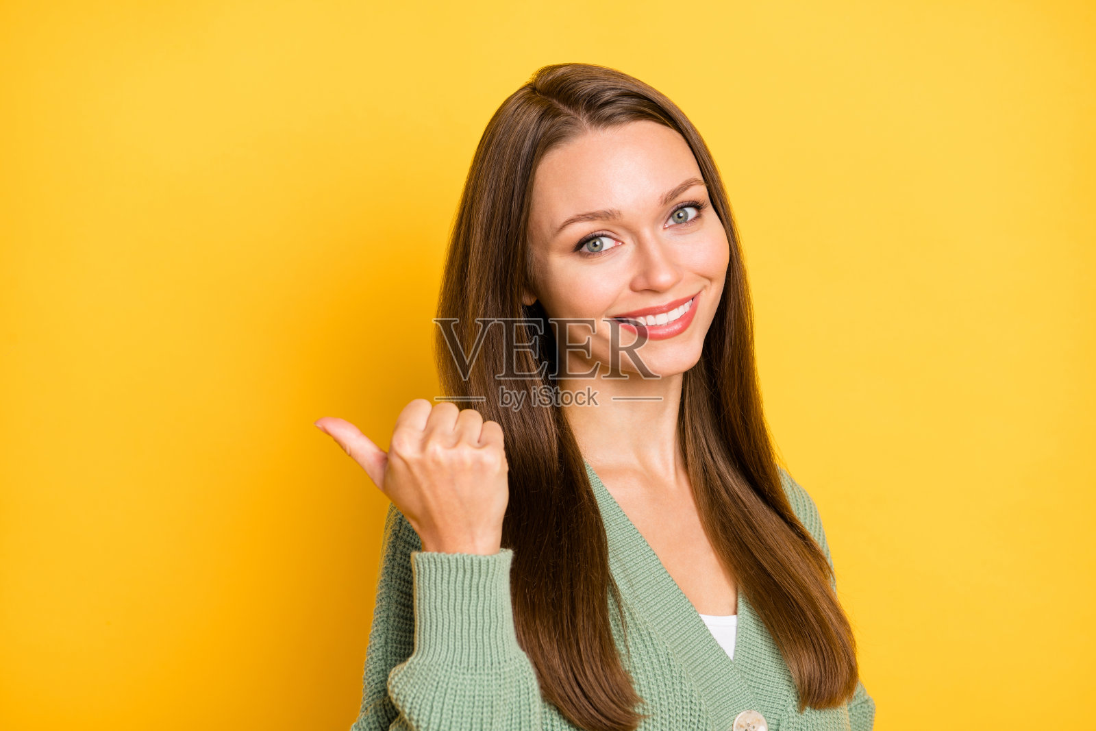微笑女孩的照片肖像，拇指指向身后空白处，背景为鲜艳的黄色。照片摄影图片