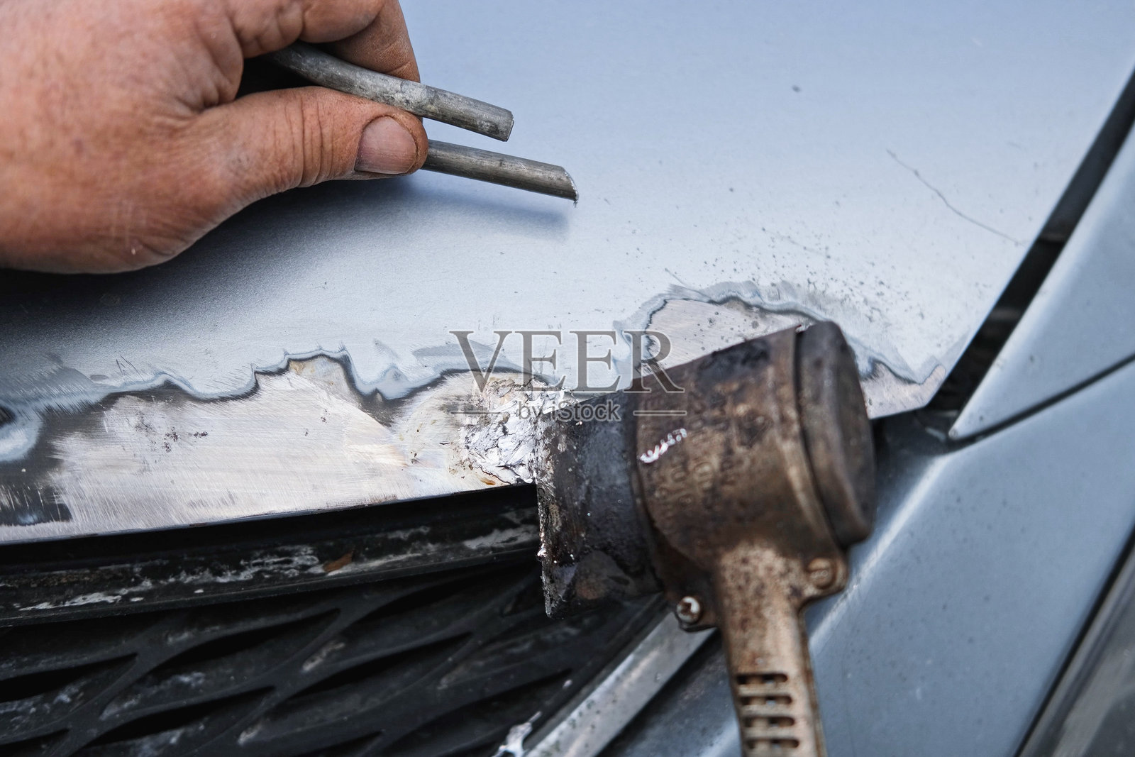 汽车修理厂。修理工使用角磨机处理更换汽车部件的焊缝。专业车身技师打磨旧漆和锈蚀。锈蚀损坏。生锈的汽车。工具特写的手部。照片摄影图片