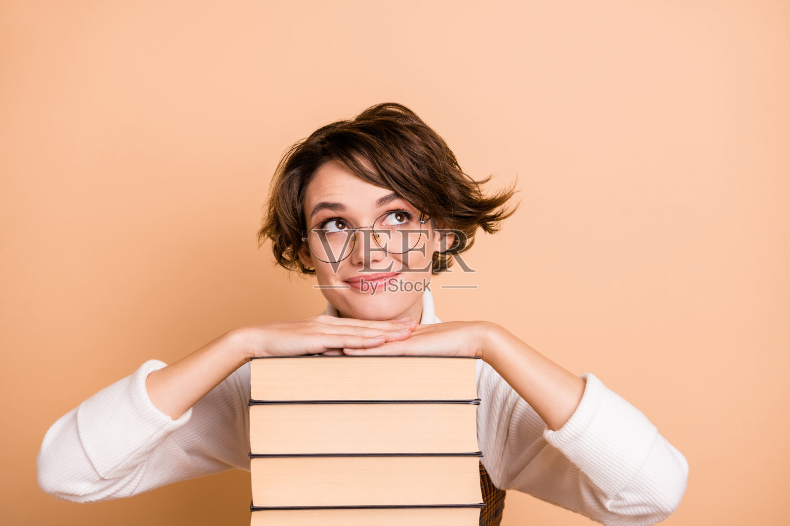 学校女孩在书堆旁做梦，目光呆滞，背景为柔和的米色。照片摄影图片