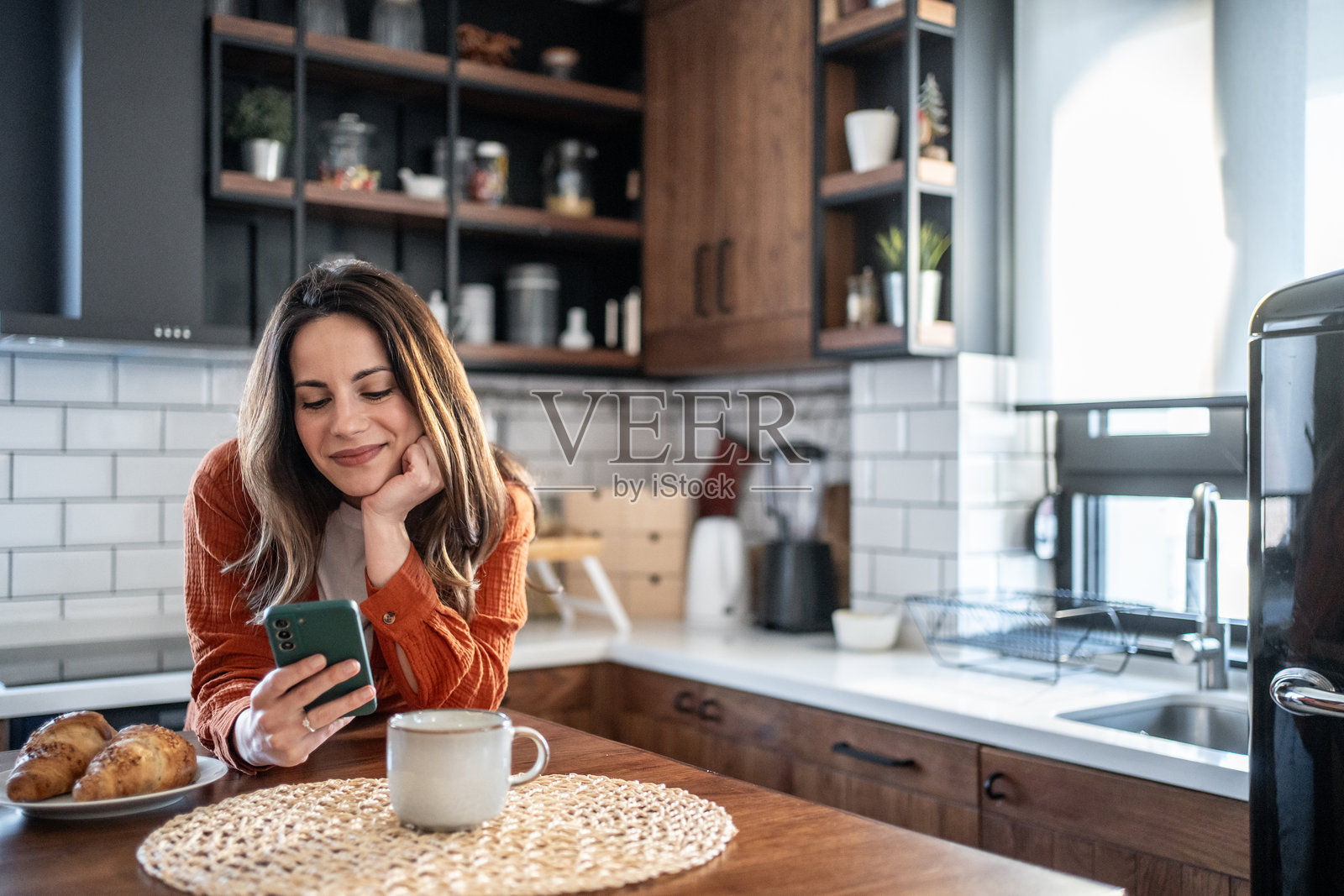 微笑的女性在现代厨房里用智能手机吃早餐照片摄影图片