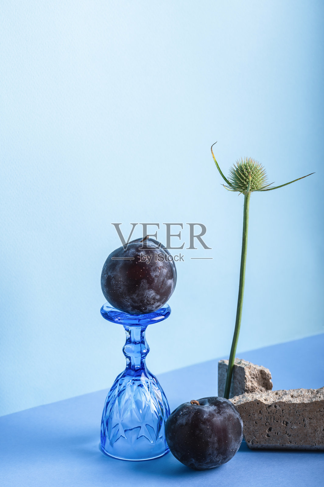 静物画：蓝色背景上的成熟李子和玻璃杯。照片摄影图片