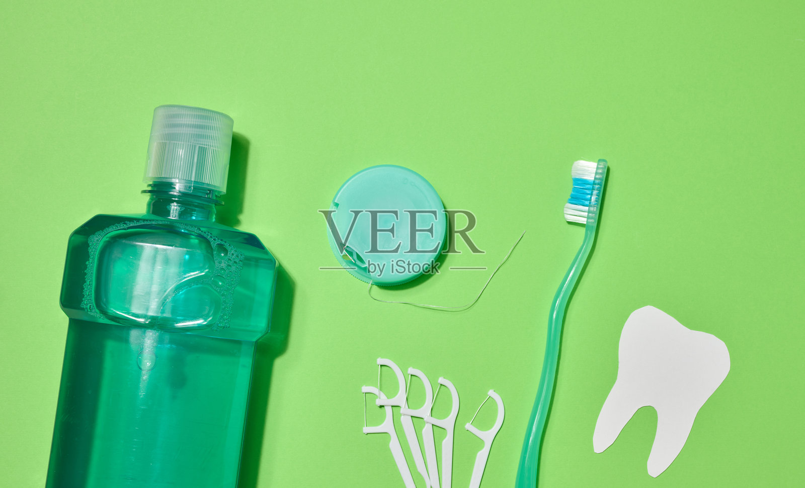 绿色牙刷、漱口水瓶、牙线盒中的牙线、绿色背景上的塑料牙线夹。照片摄影图片