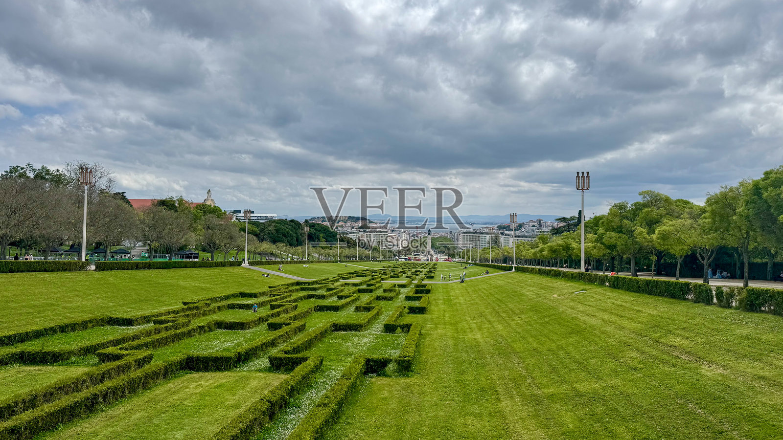 广阔的绿色公园，修剪整齐的树篱，背景是里斯本的建筑，映衬着戏剧性的多云天空。照片摄影图片