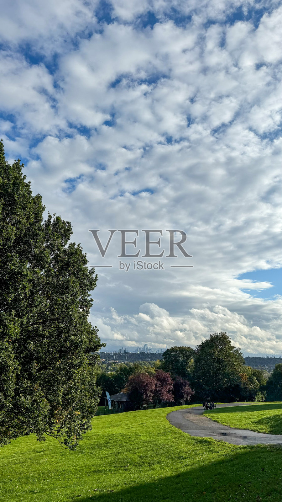 广阔的蓝天上点缀着蓬松的白云，宁静的绿色公园景观与伦敦天际线在金色时光中交相辉映。照片摄影图片