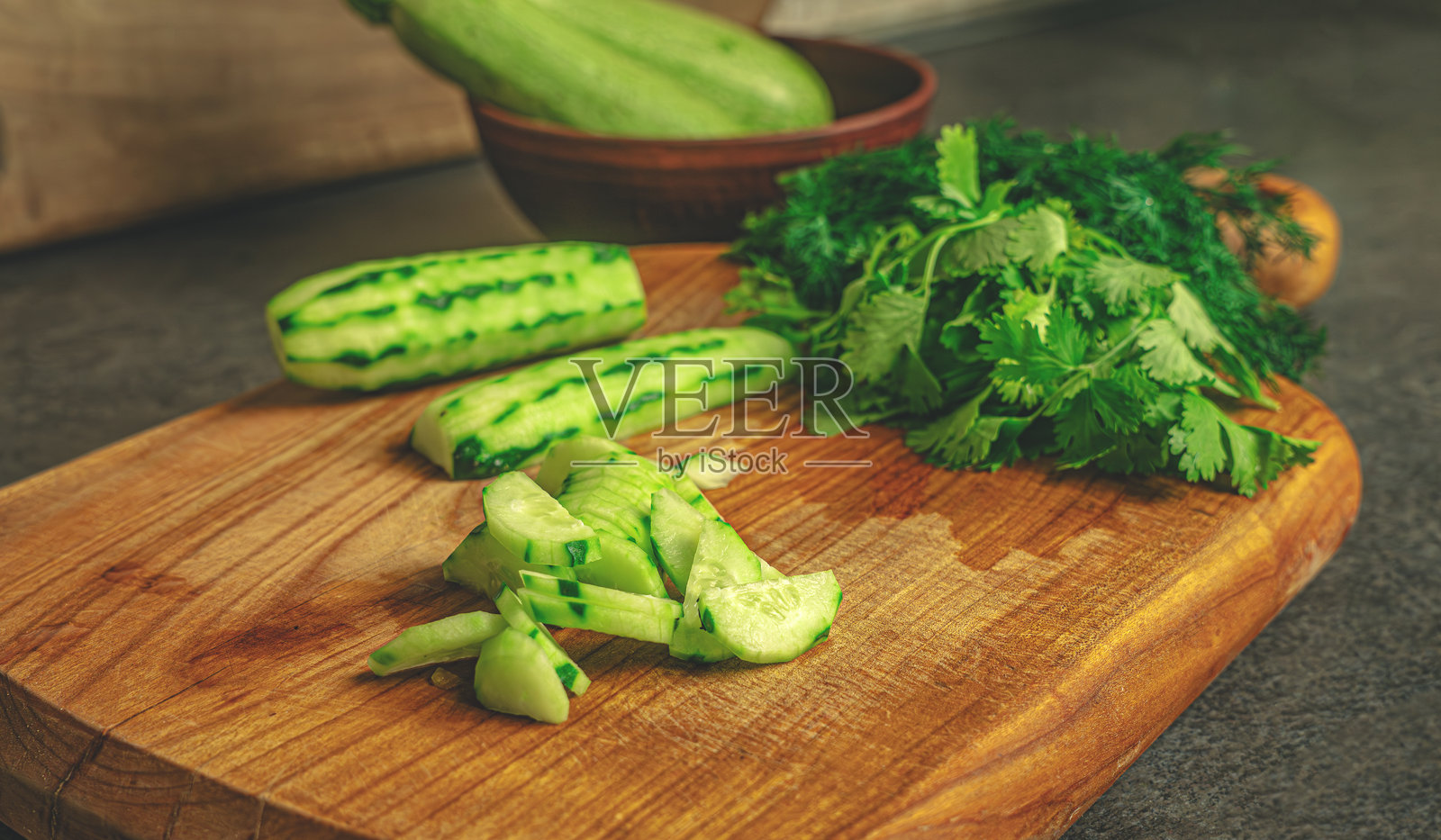 在樱桃木切菜板上，新鲜的香草和去皮的黄瓜被准备成一道健康菜肴。乡村风格的厨房表面和自然的构图营造出温暖、有机的氛围，适合生活方式和烹饪视觉。照片摄影图片