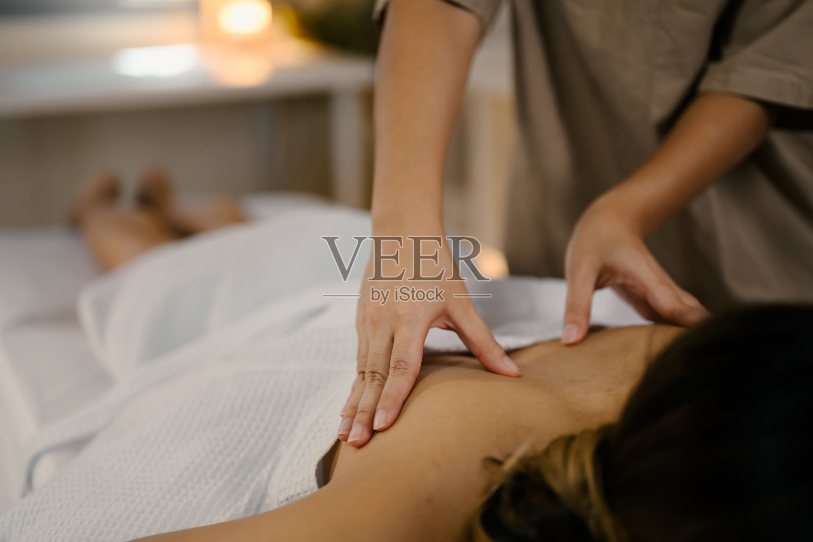 女性客户在治疗台上享受舒缓的身体按摩，环境宁静。健康概念照片摄影图片