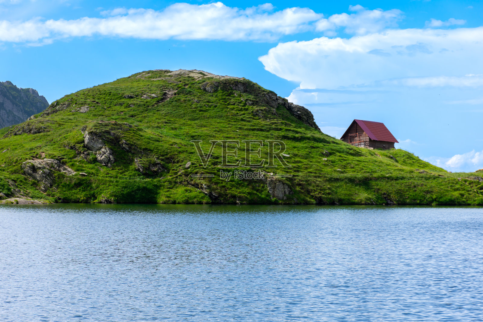 一座迷人的小房子坐落在山丘上，俯瞰着宁静的湖泊。照片摄影图片