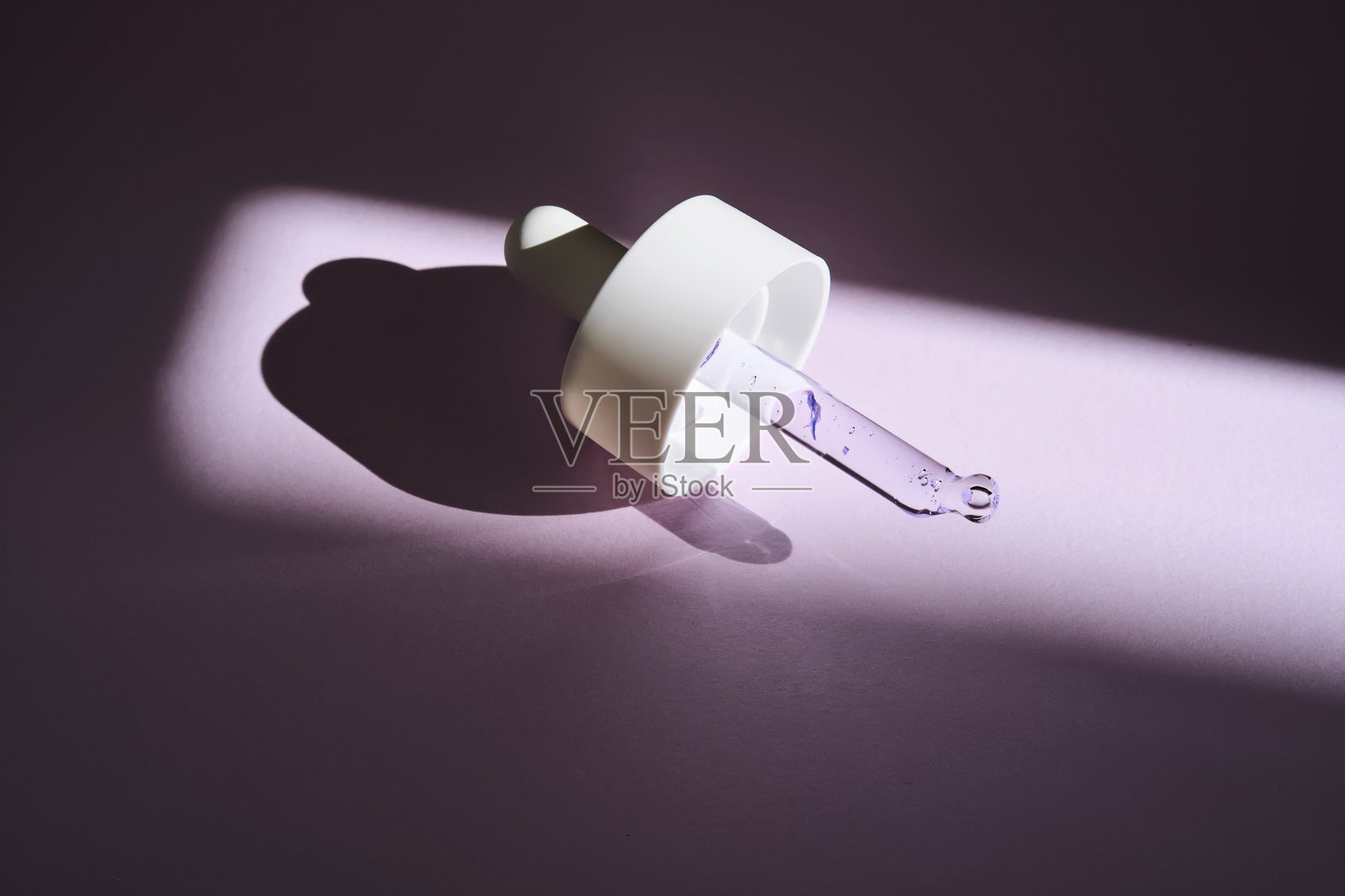 紫色背景下阳光照射下的带有血清的移液器。照片摄影图片