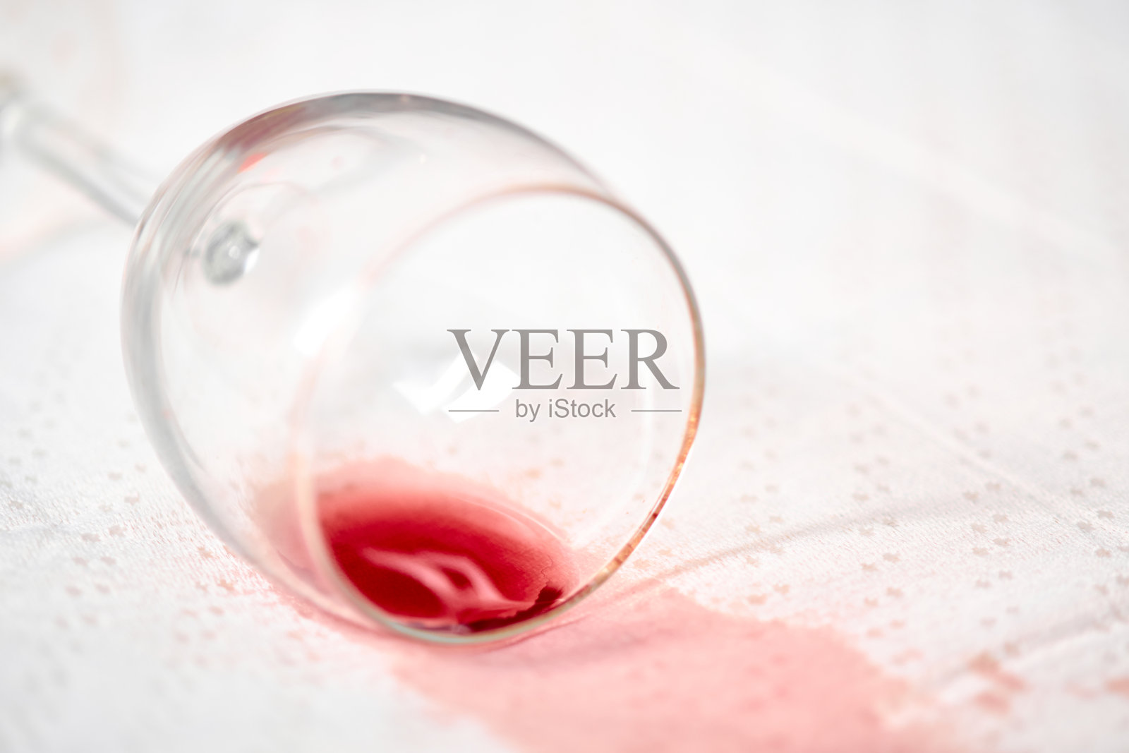 红酒洒在白色桌布上，旁边有一个倾倒的酒杯照片摄影图片