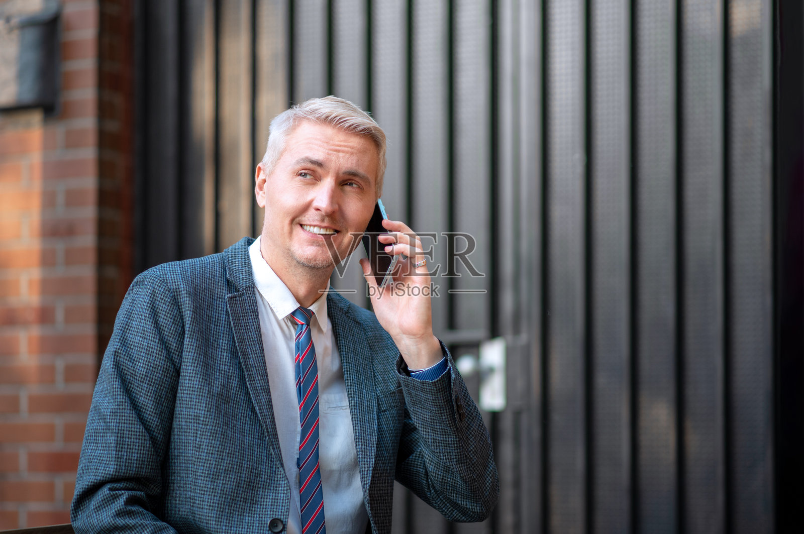 微笑的商人在户外穿着西装和领带打电话。照片摄影图片
