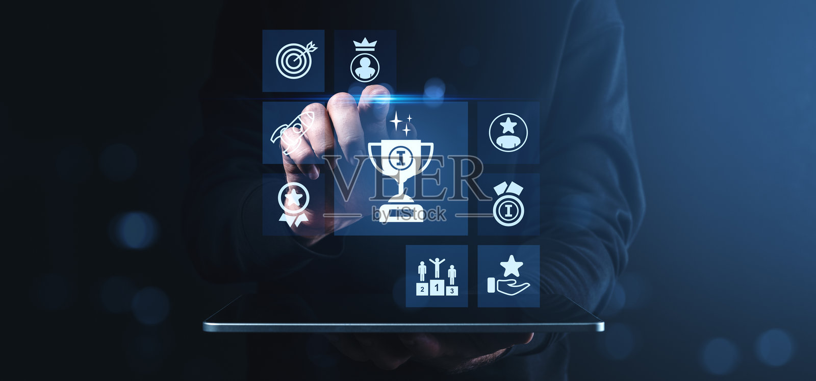 男子在平板屏幕上与象征成功、奖励和绩效评估的数字成就图标互动，展现现代科技环境。照片摄影图片